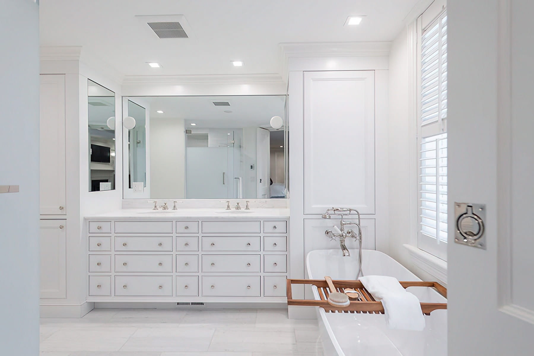 Bright white bathroom with a freestanding tub, double vanity, custom cabinetry, and plantation shutters at the Chestnut Street Residence in Boston.