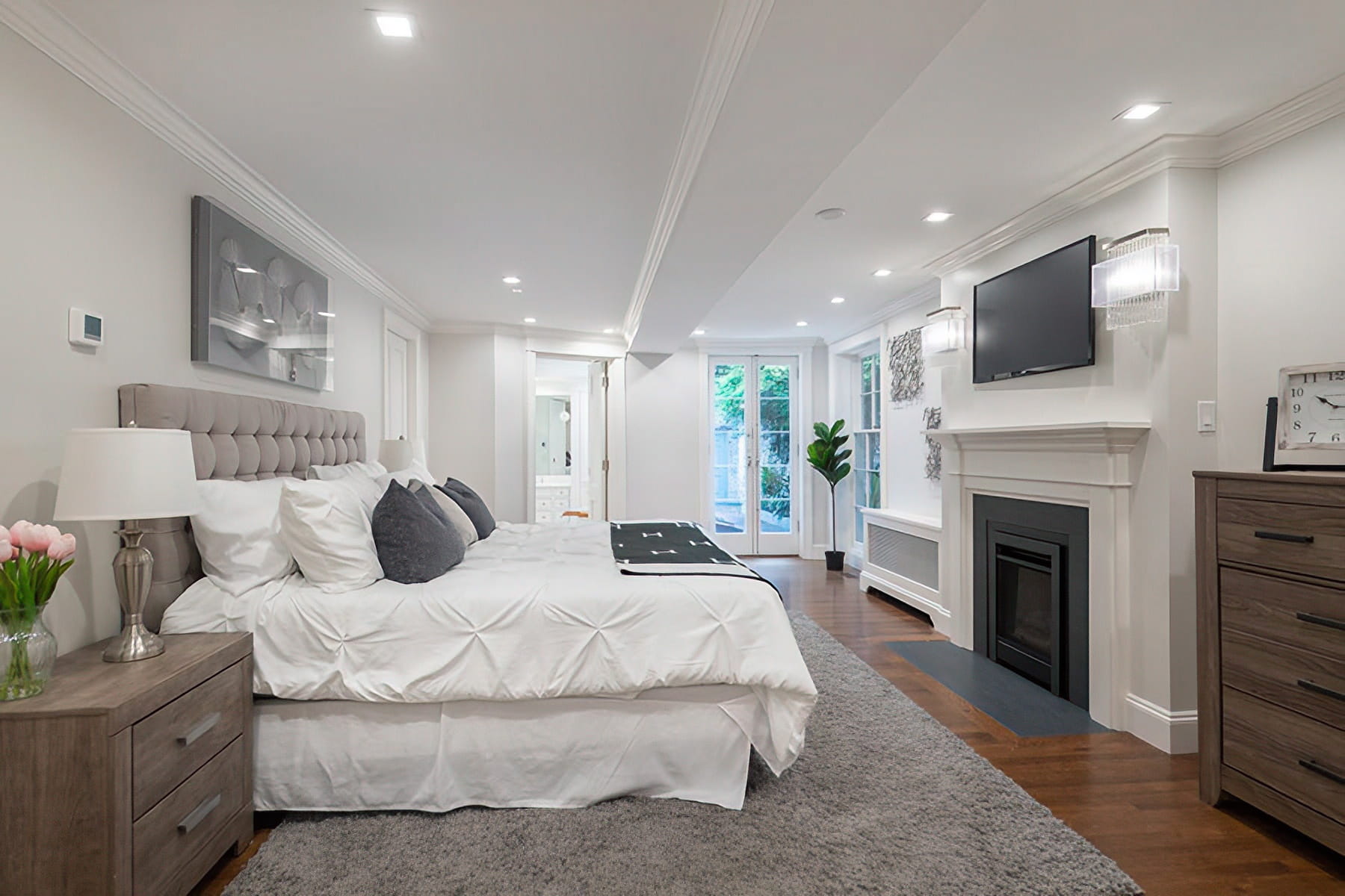 Primary bedroom with a fireplace, tufted bed, custom millwork, and French doors opening to the courtyard at the Chestnut Street Residence in Boston.