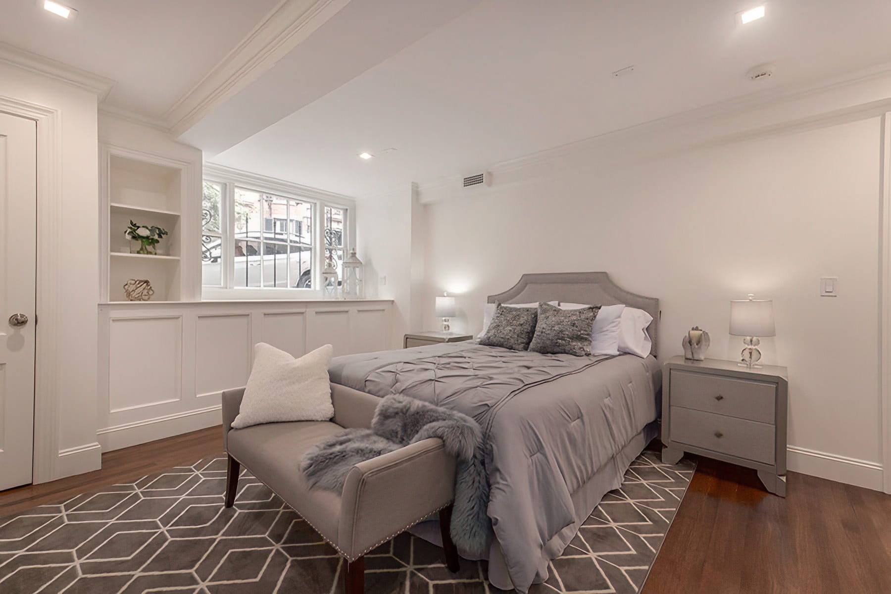Lower-level bedroom with gray furnishings, paneled walls, built-in shelving, and wood flooring at the Chestnut Street Residence in Boston.
