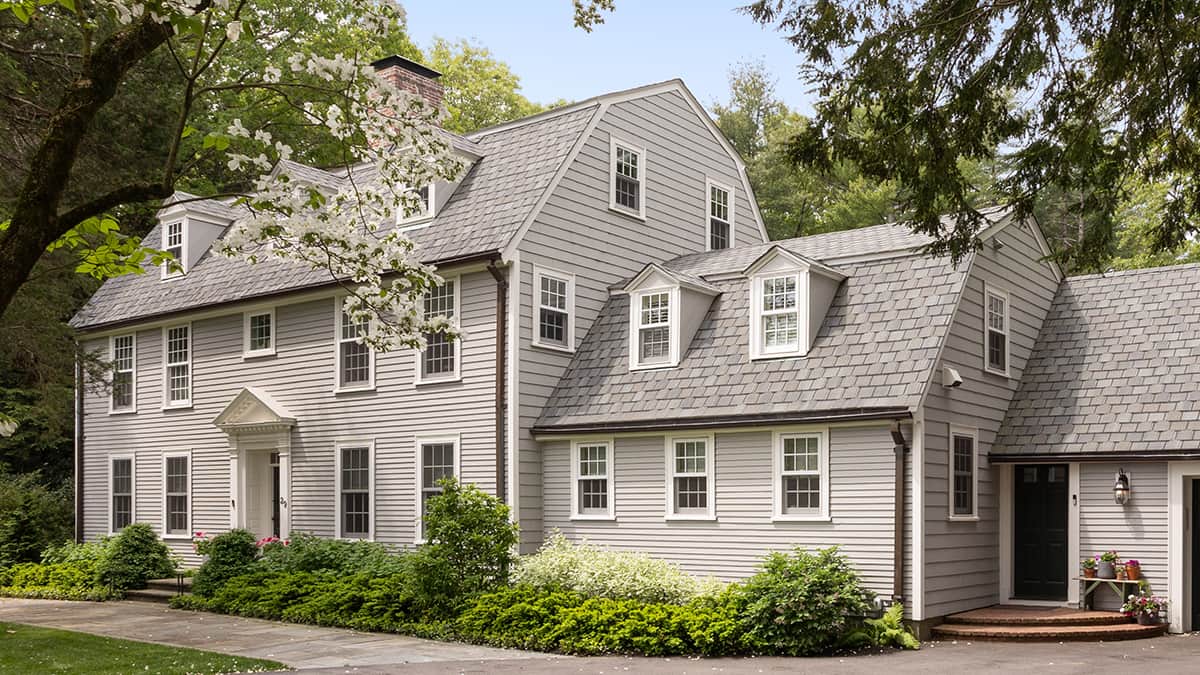 Custom residential architecture featuring a traditional New England home with dormer windows, slate-style roof, and landscaped grounds