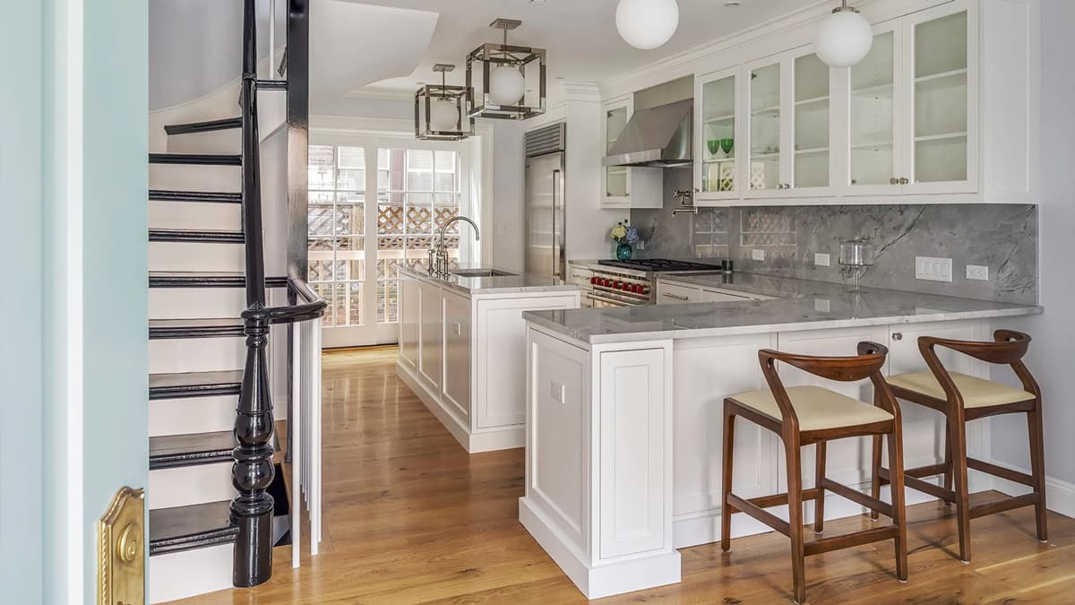 Renovated kitchen at the South Russell Street Townhouse in Boston with custom white cabinetry, stone surfaces, breakfast seating, and adjacent stairway